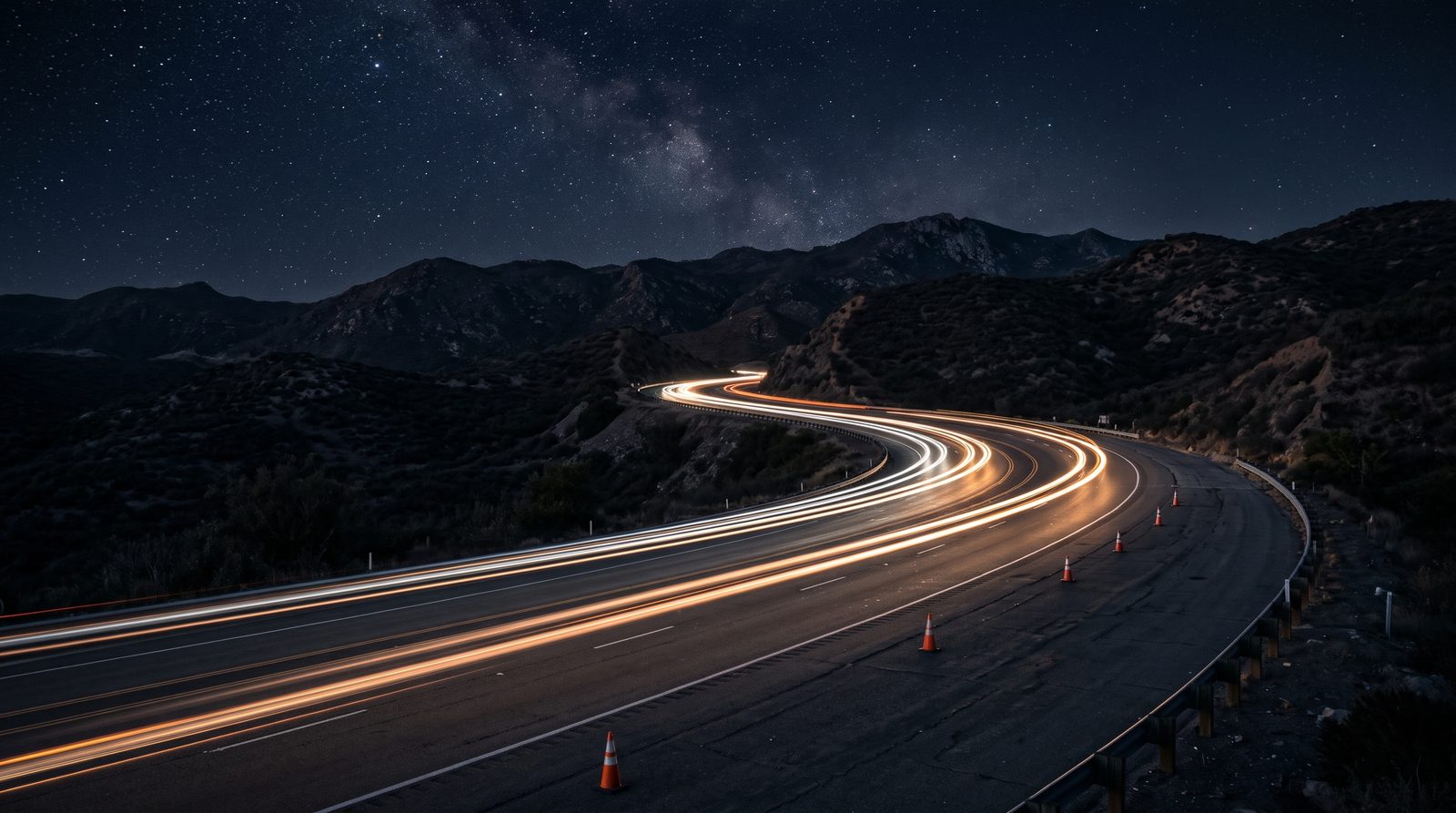 Light trails sweeping along an empty highway curve at night under a starry sky in the East County hills