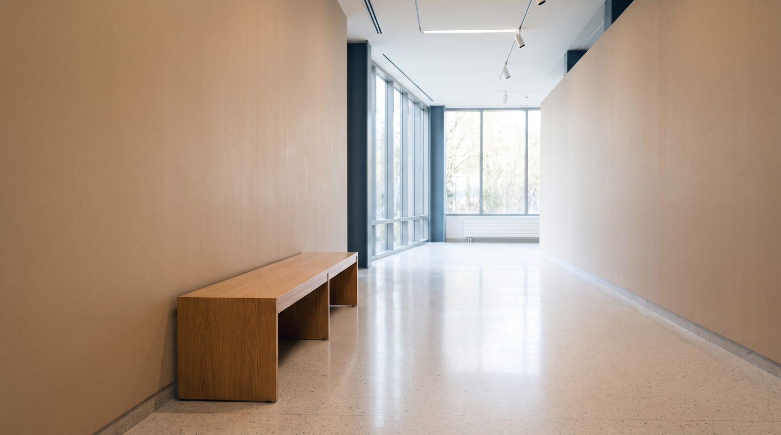 An empty bright corridor with a plain wooden bench against a warm beige wall